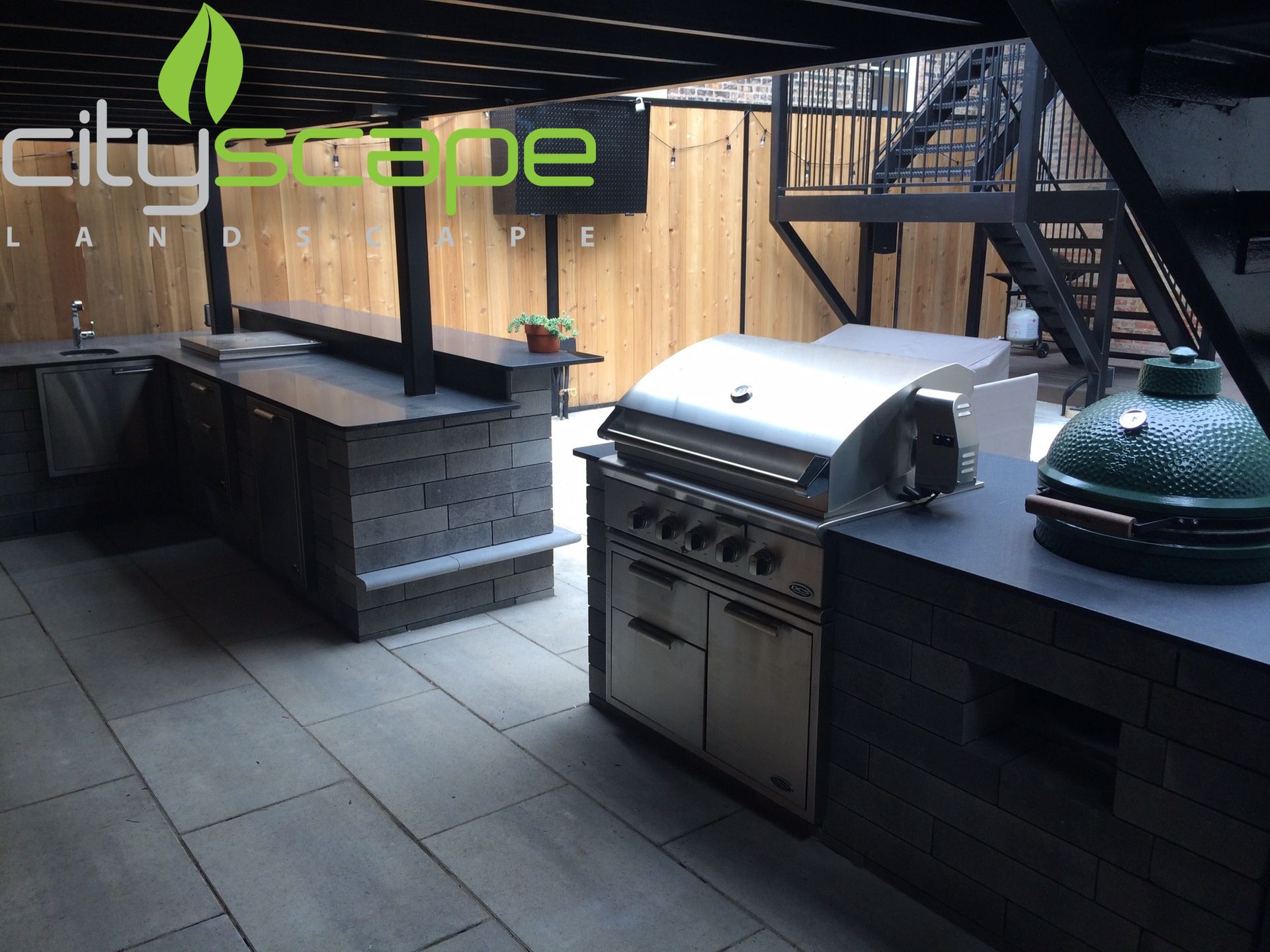 Outdoor kitchen with built-in grill, countertops, and a Big Green Egg on a patio.