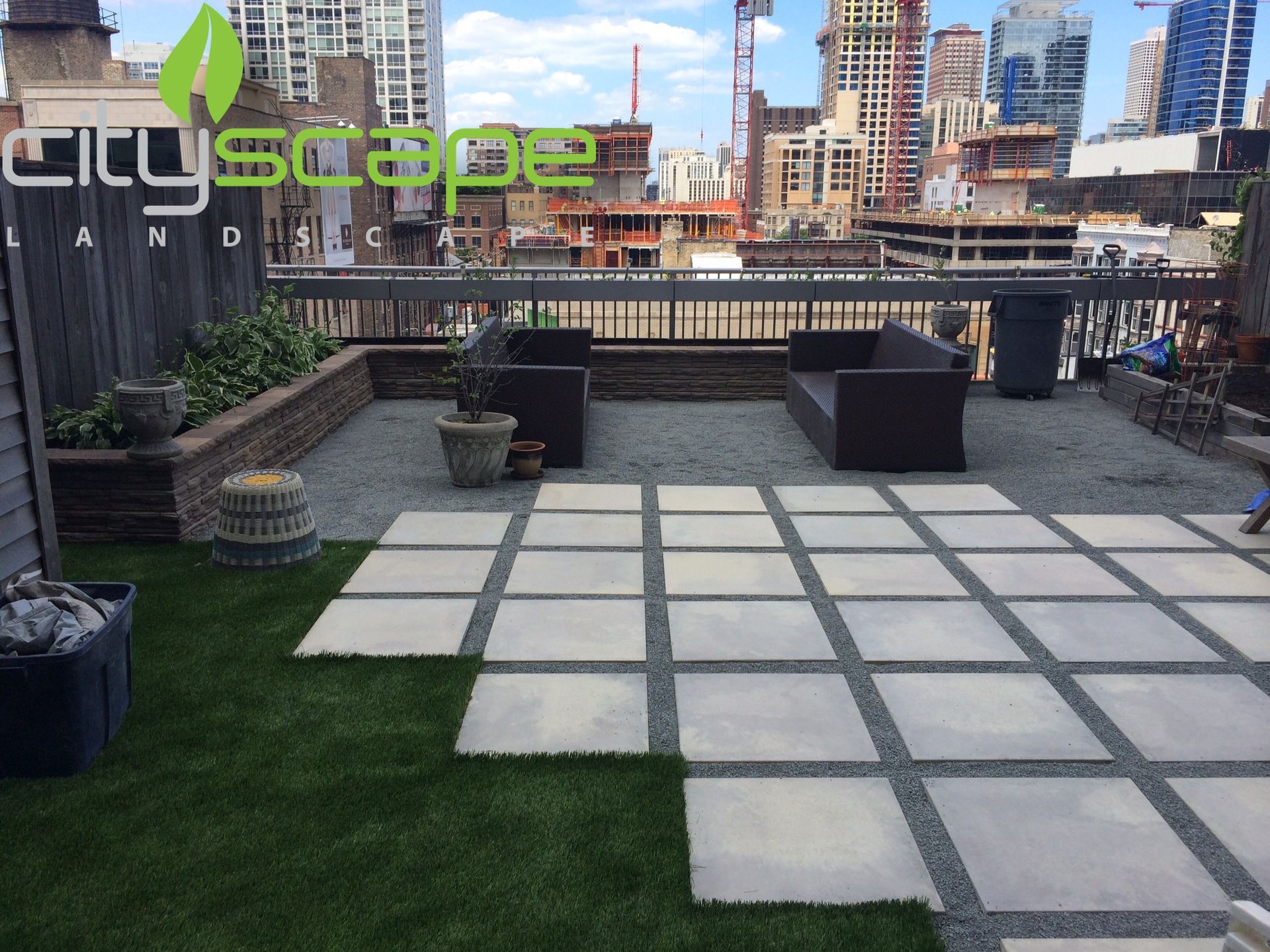 Rooftop patio with pavers, gravel, artificial turf, and modern furniture; cityscape background.