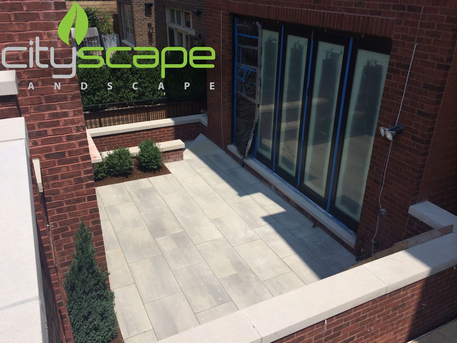 A paved outdoor patio with red brick walls, large glass doors, and small bushes.
