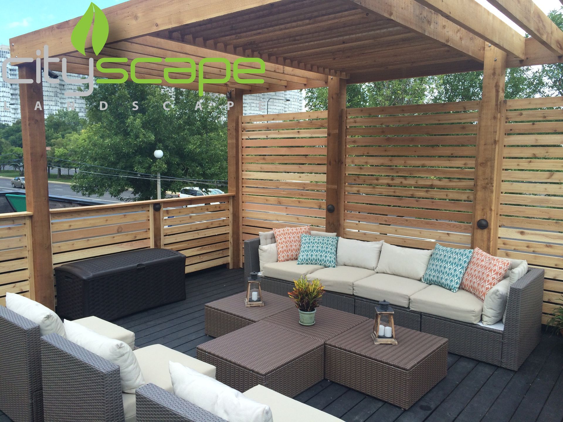 Outdoor seating area with a pergola and wooden privacy screen. Beige cushions on brown wicker furniture.