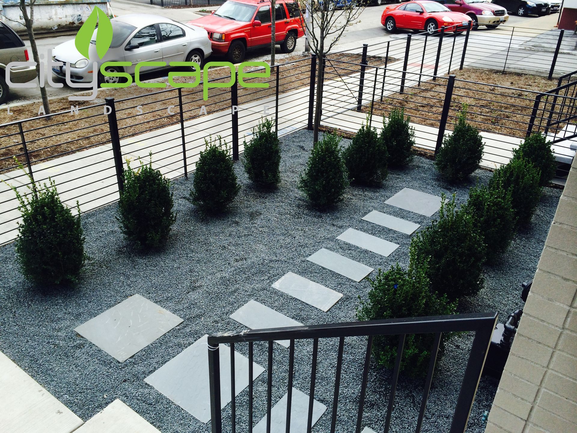 Small garden bed with dark gravel, square stone path, and trimmed evergreen shrubs.
