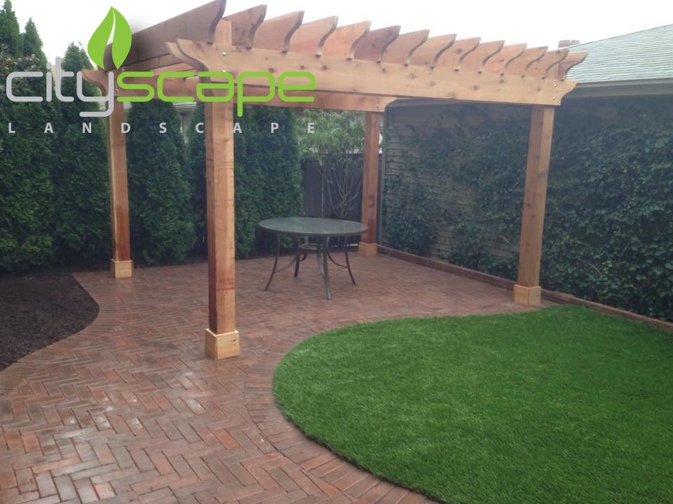 Outdoor patio with brick pavers, pergola, and green turf.