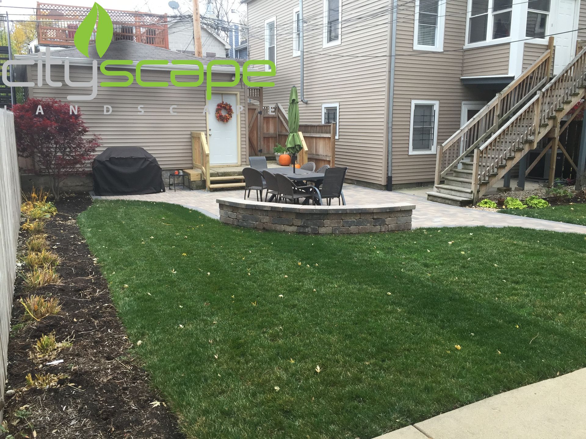 Backyard patio with lawn, dining set, grill, and low retaining wall.