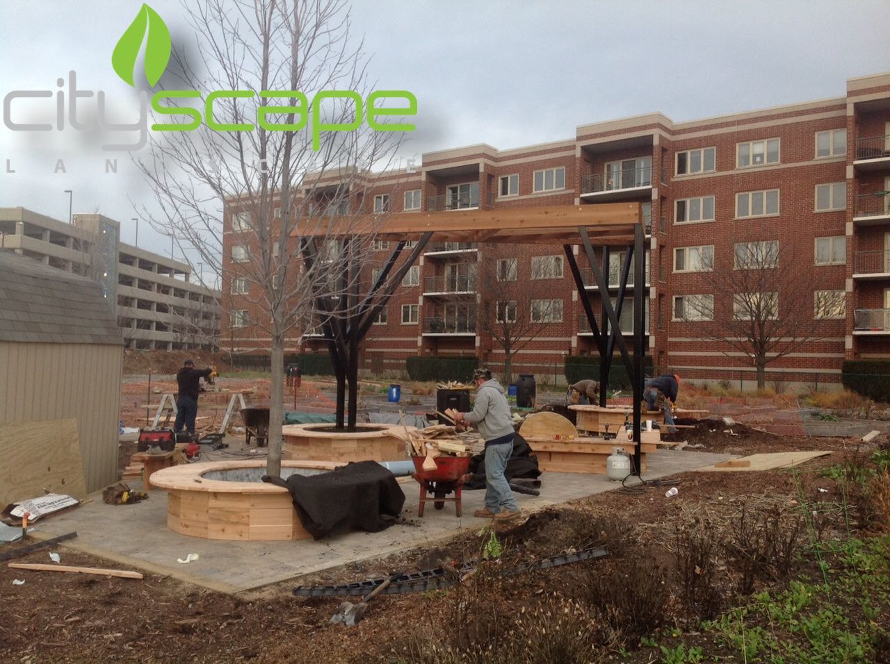 Construction site with workers building a wooden pergola in front of a brick building.