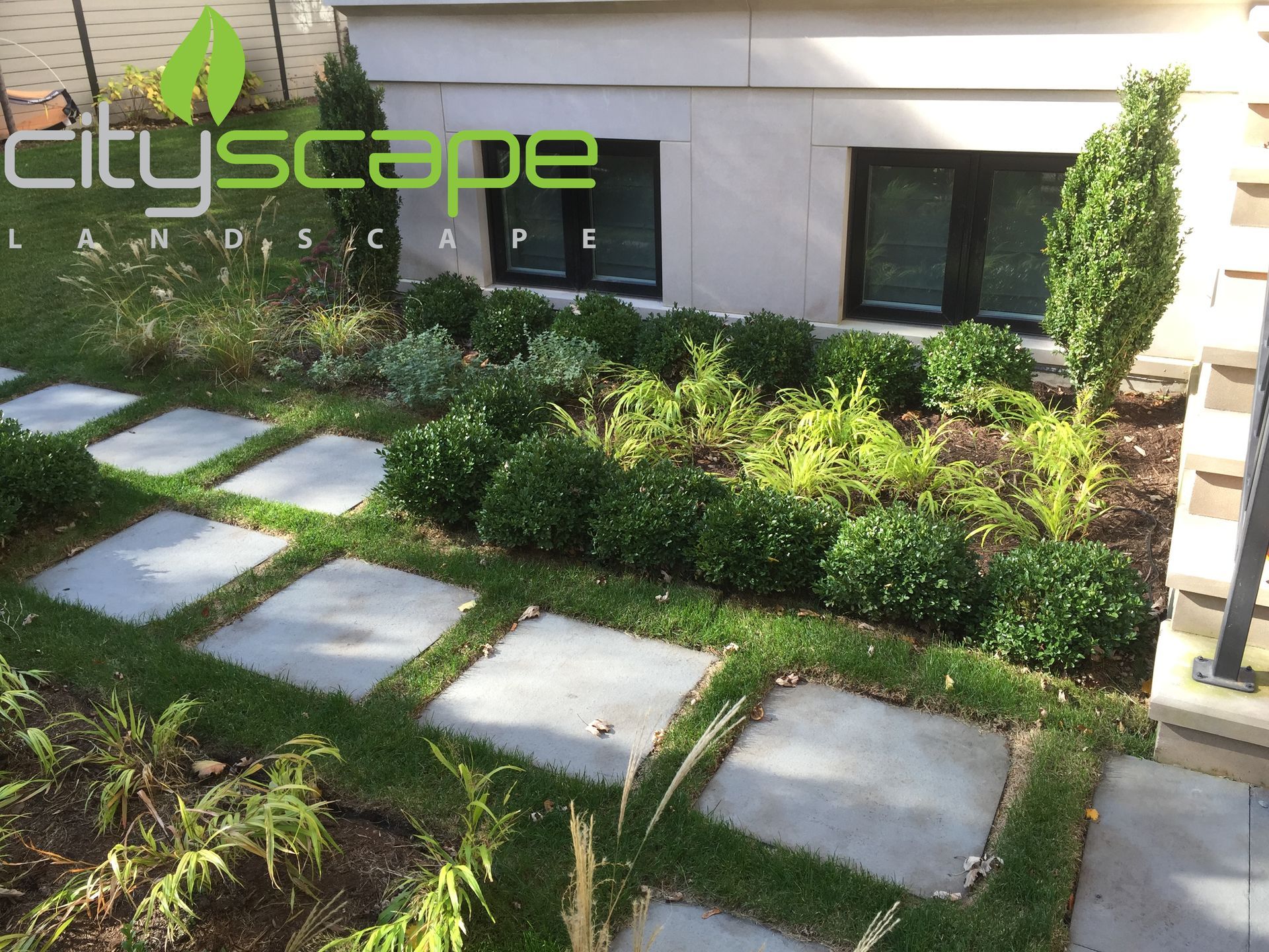 Stone path in a landscaped garden with trimmed hedges and green foliage against a building.