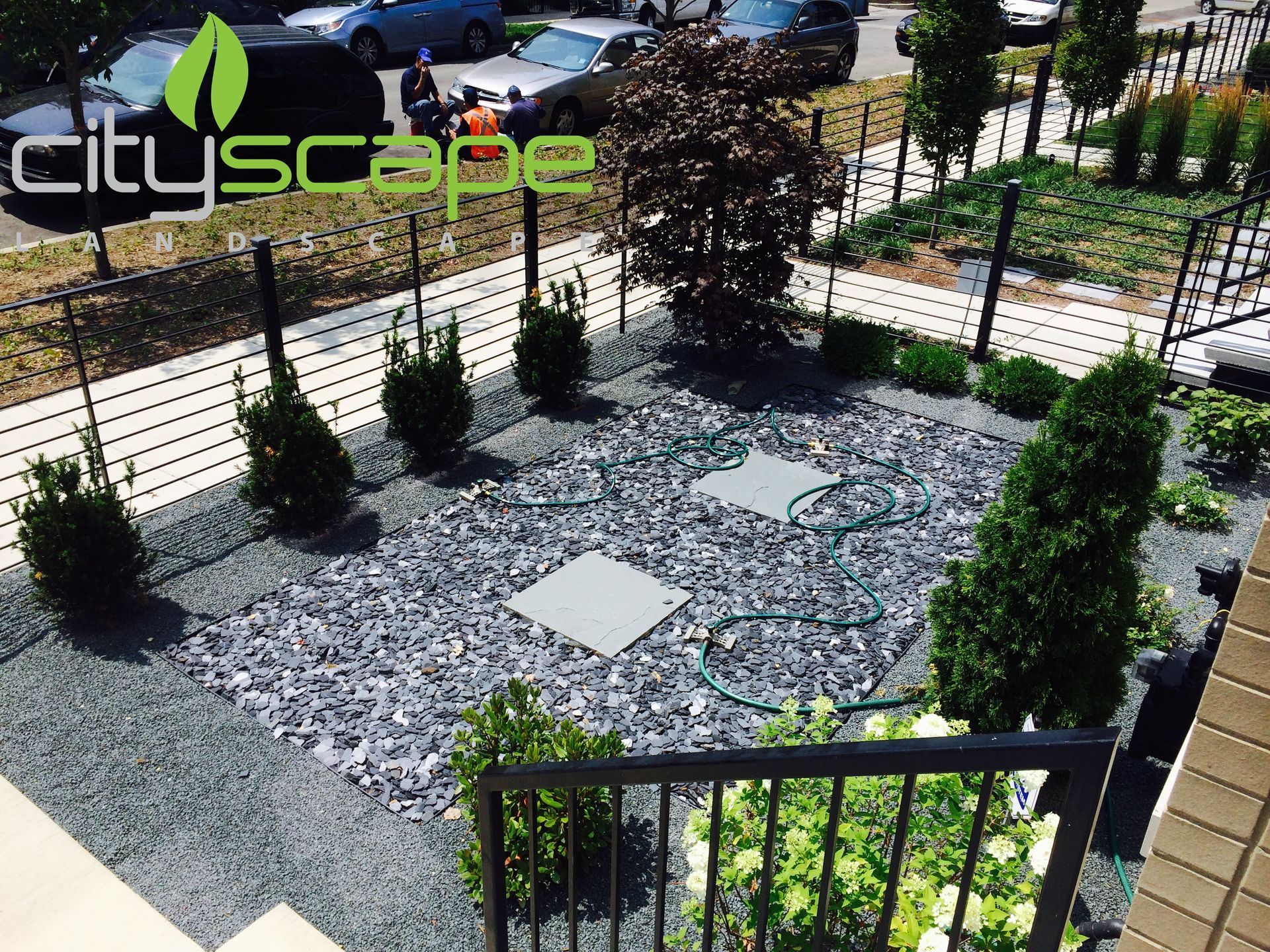 Landscaped garden with dark gravel, shrubs, and square utility access covers.