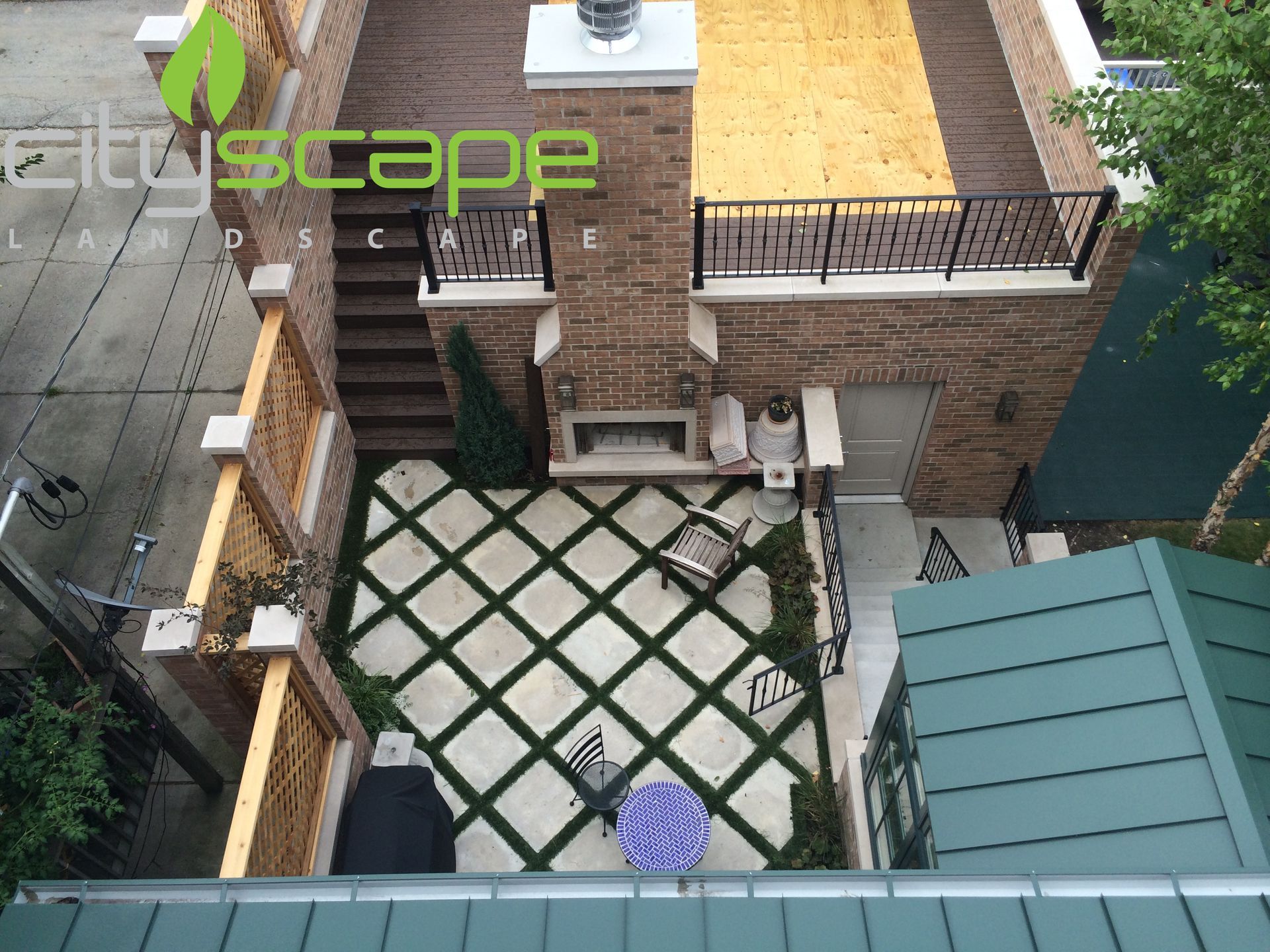 Overhead view of a rooftop patio with geometric green grass and concrete design, fireplace, seating, and a stairway.