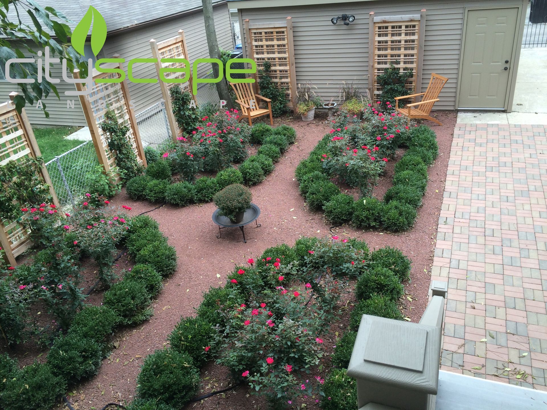 A well-manicured garden with boxwood hedges, red mulch, and wooden lattice screens.