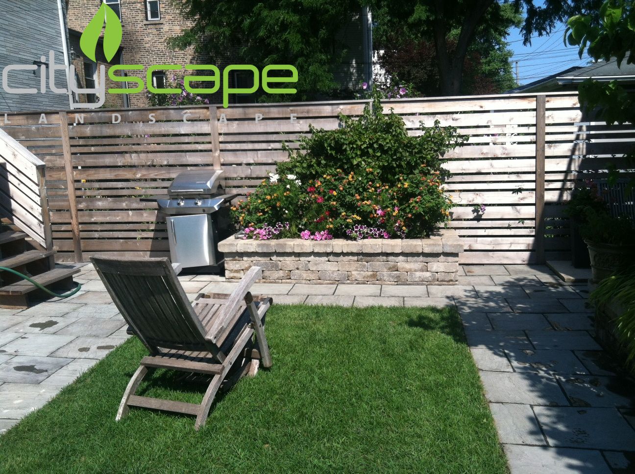 Backyard with grill, lounge chair, lawn, brick patio, and wooden fence.