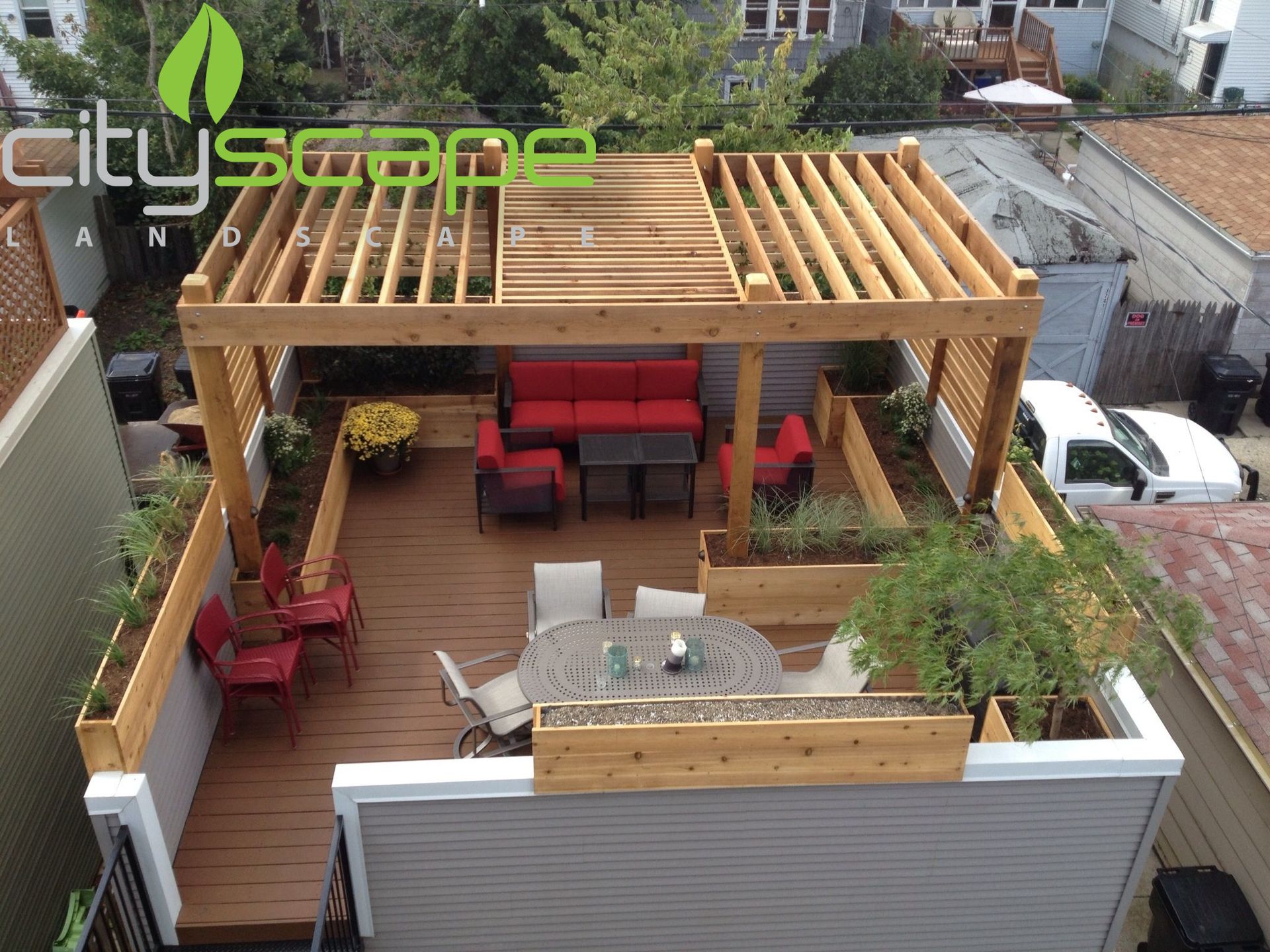 Rooftop deck with pergola and seating, including a red couch and dining table, with built-in planters.