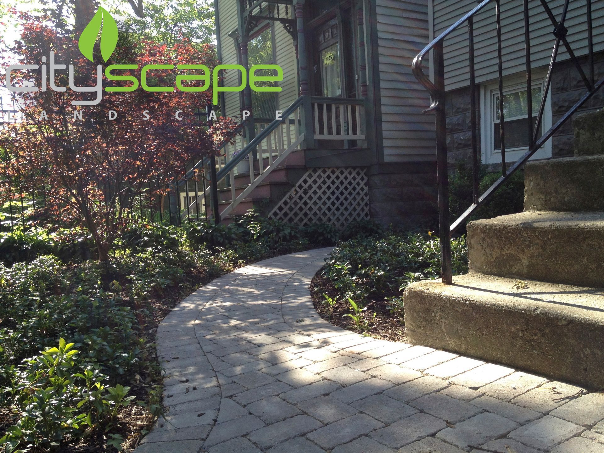 Brick pathway leads to house with porch, lush garden on either side.