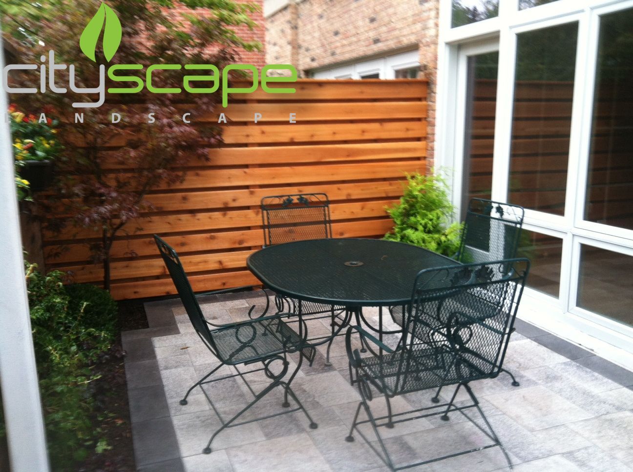 Outdoor patio with black table and chairs, wood fence, and glass door.