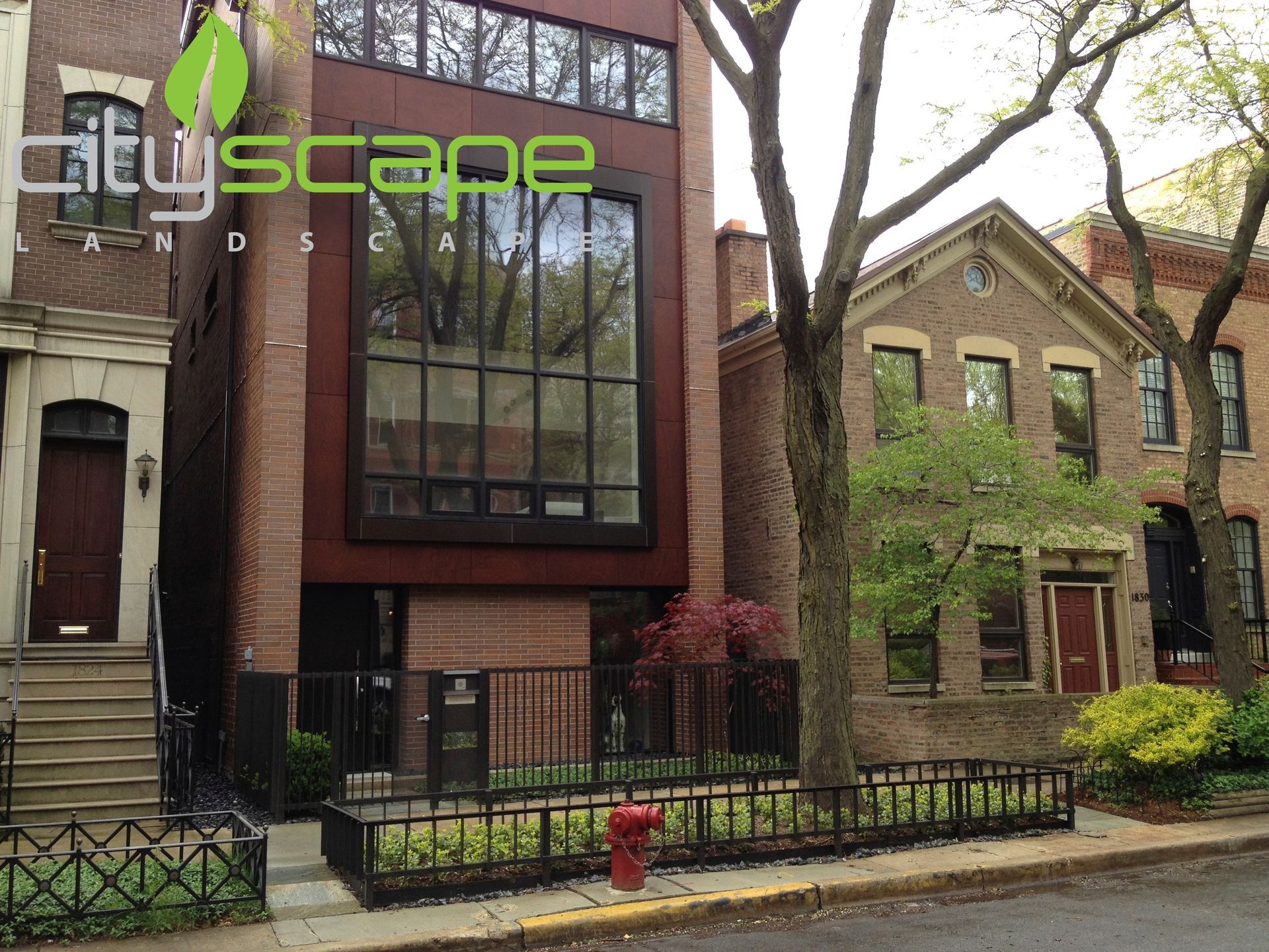 Row of brick townhouses. One has a large dark window, the others have doors and trees.