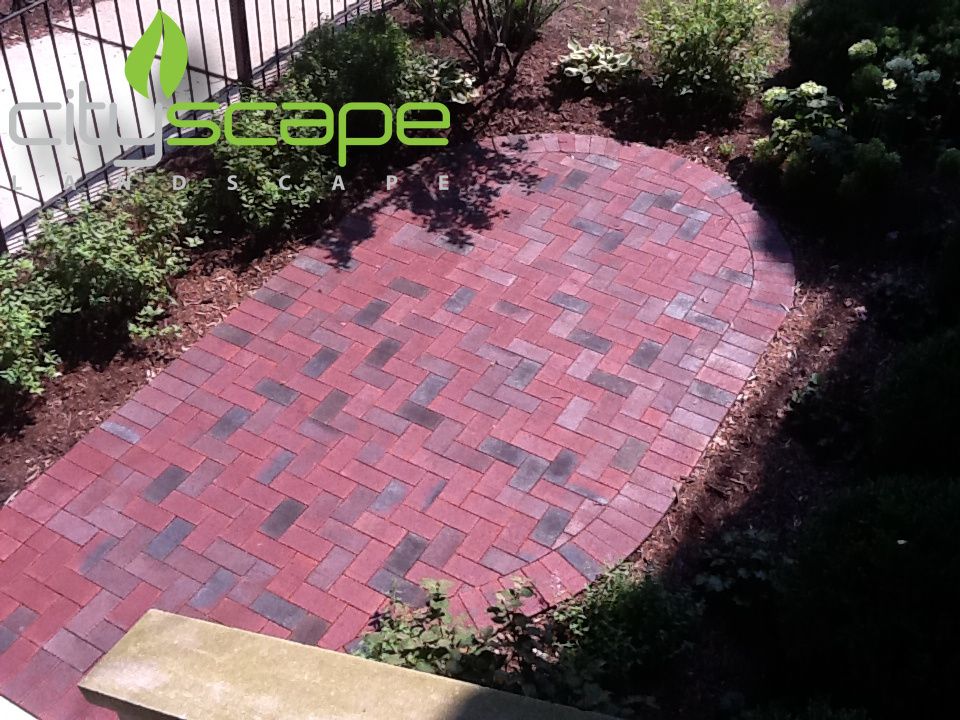 Red brick patio in herringbone pattern, surrounded by plants and mulch.