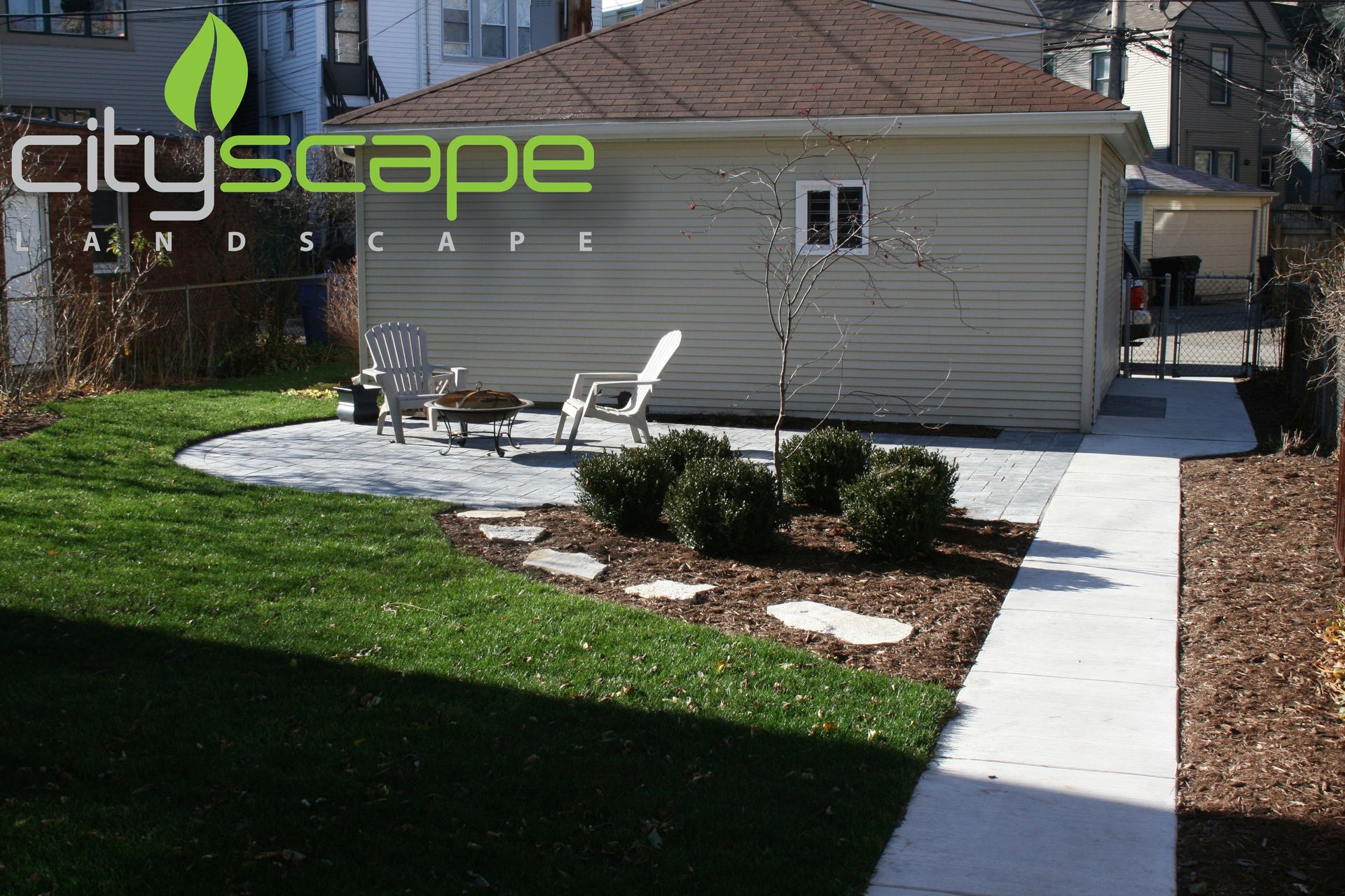 Backyard landscape design with patio, lawn, and garage. Includes chairs, shrubs, and a walkway.