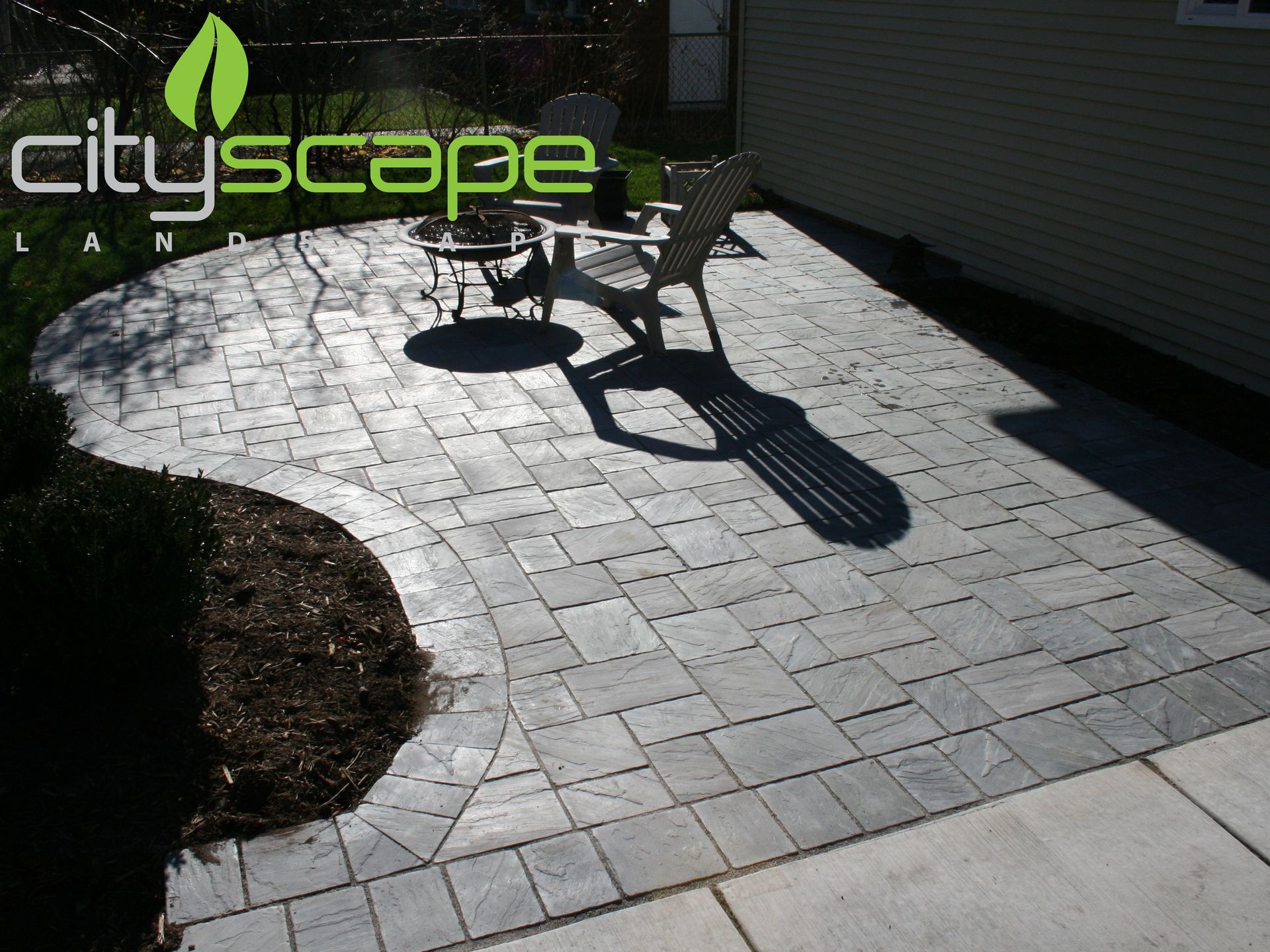 Brick patio with furniture, next to a beige house, with a curving edge.