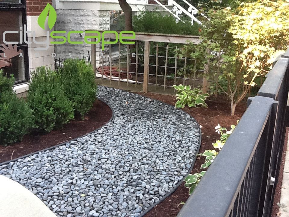 A winding stone path bordered by bushes and mulch in front of a building.