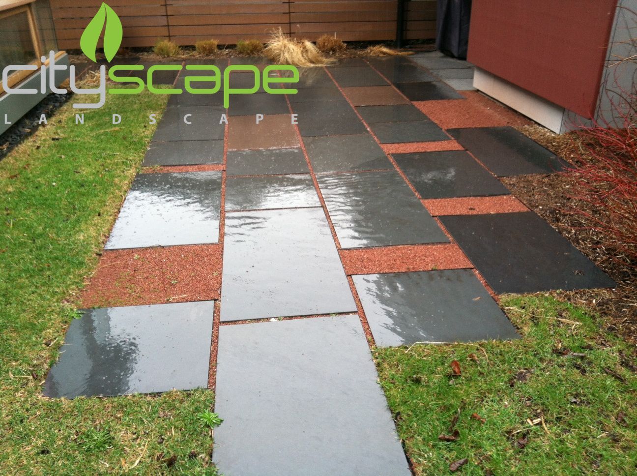 Pathway of dark gray stone and red gravel in a lawn, next to a building.