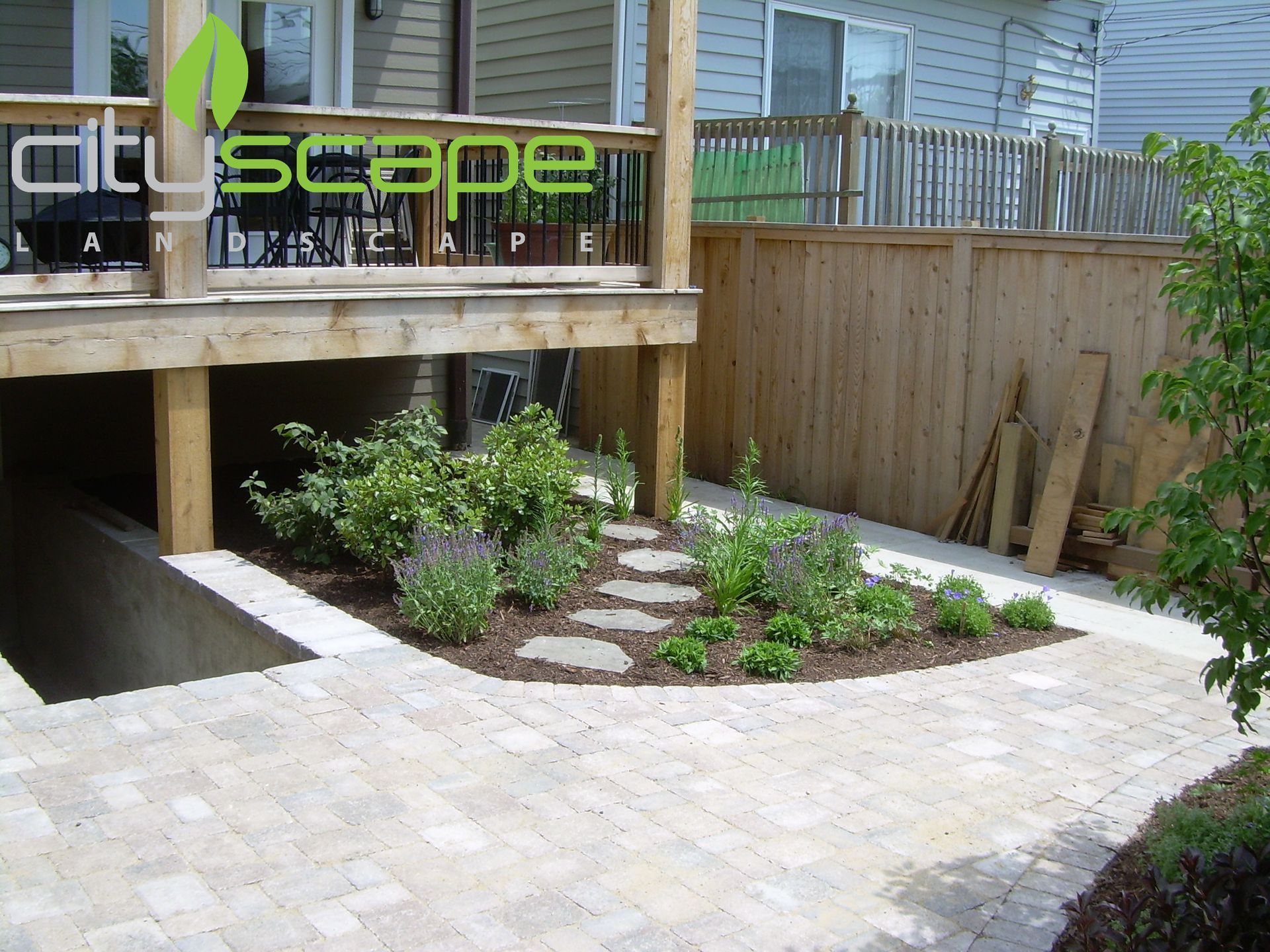 Backyard landscaping with stone path, wooden deck, and planted shrubs.