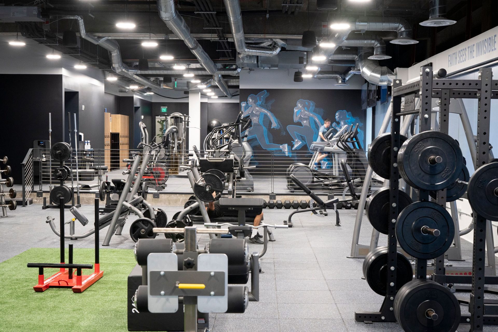 A large gym filled with lots of exercise equipment and a mural on the wall.
