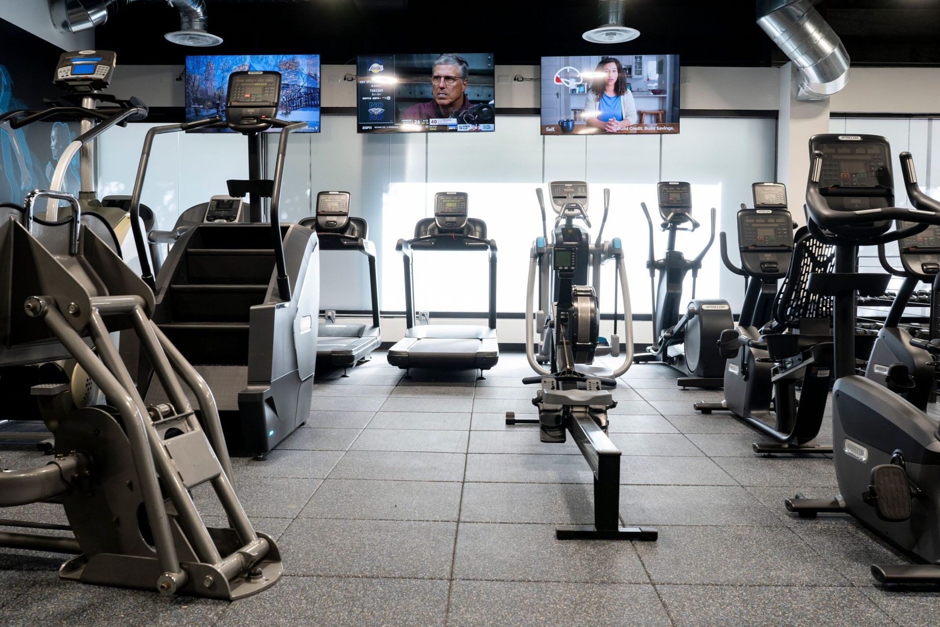 A gym filled with lots of exercise equipment and televisions.