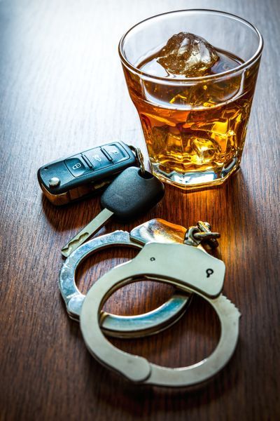 A pair of handcuffs , a car key , and a glass of whiskey on a wooden table.