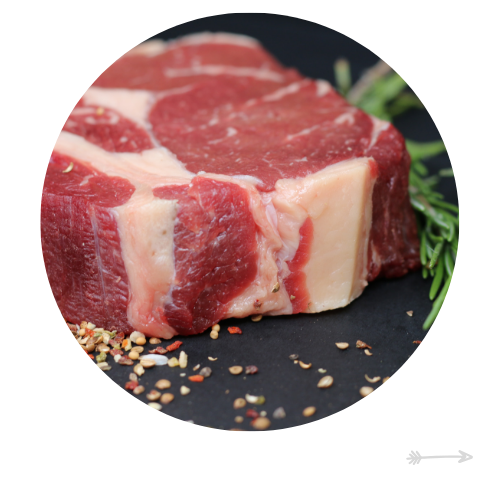 Raw ribeye steak on a dark surface with herbs and peppercorns