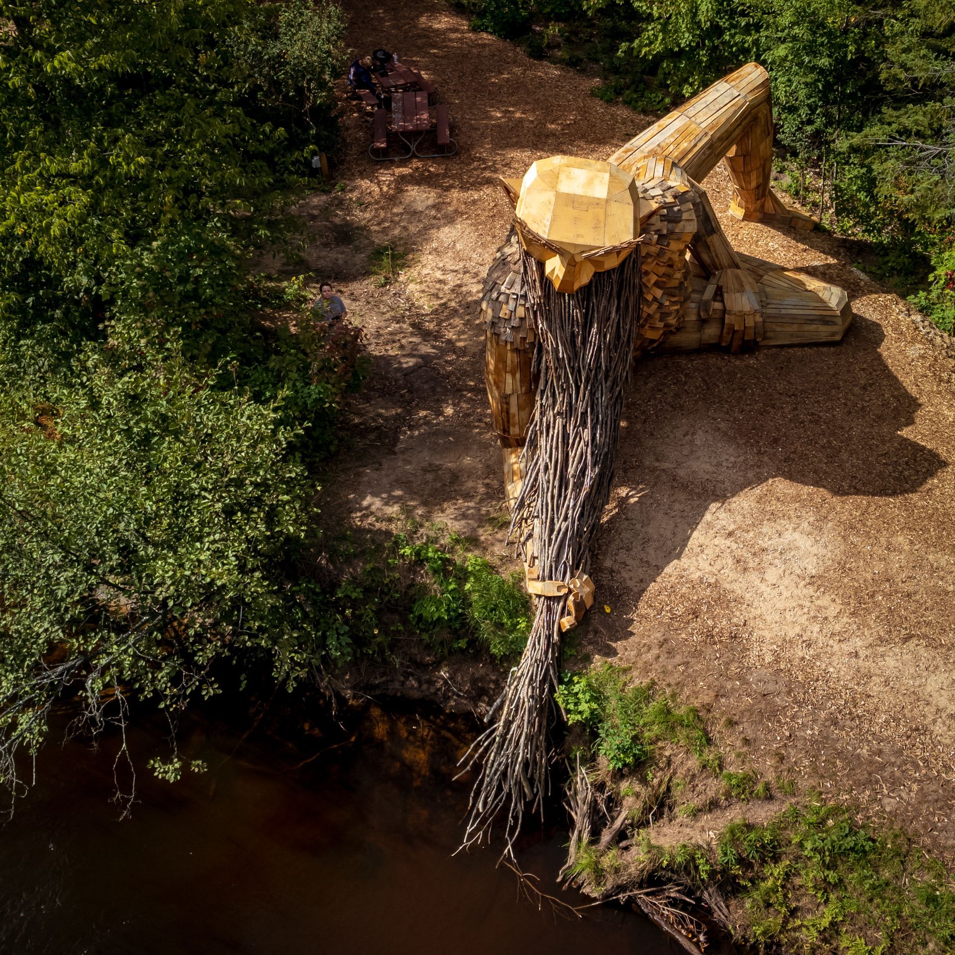 an aerial view of a wooden statue of a man standing next to a river .