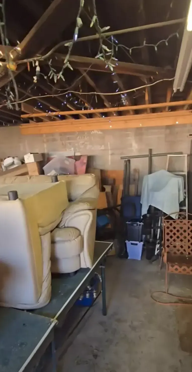 Construction materials scattered outdoors: wooden planks, beams, and bricks on a dirt ground, with trees and hills in the background.