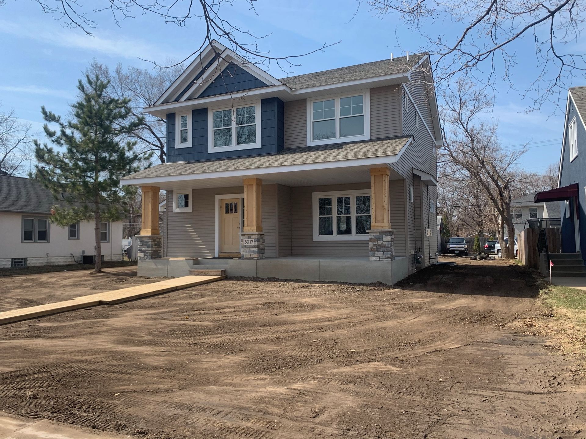 Two-story house with blue siding, tan walls, and a front porch. Unfinished yard.