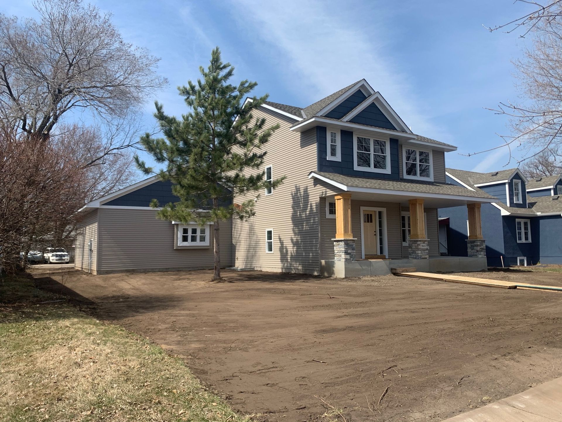 Two-story house with blue and tan siding, a porch, and a bare yard.