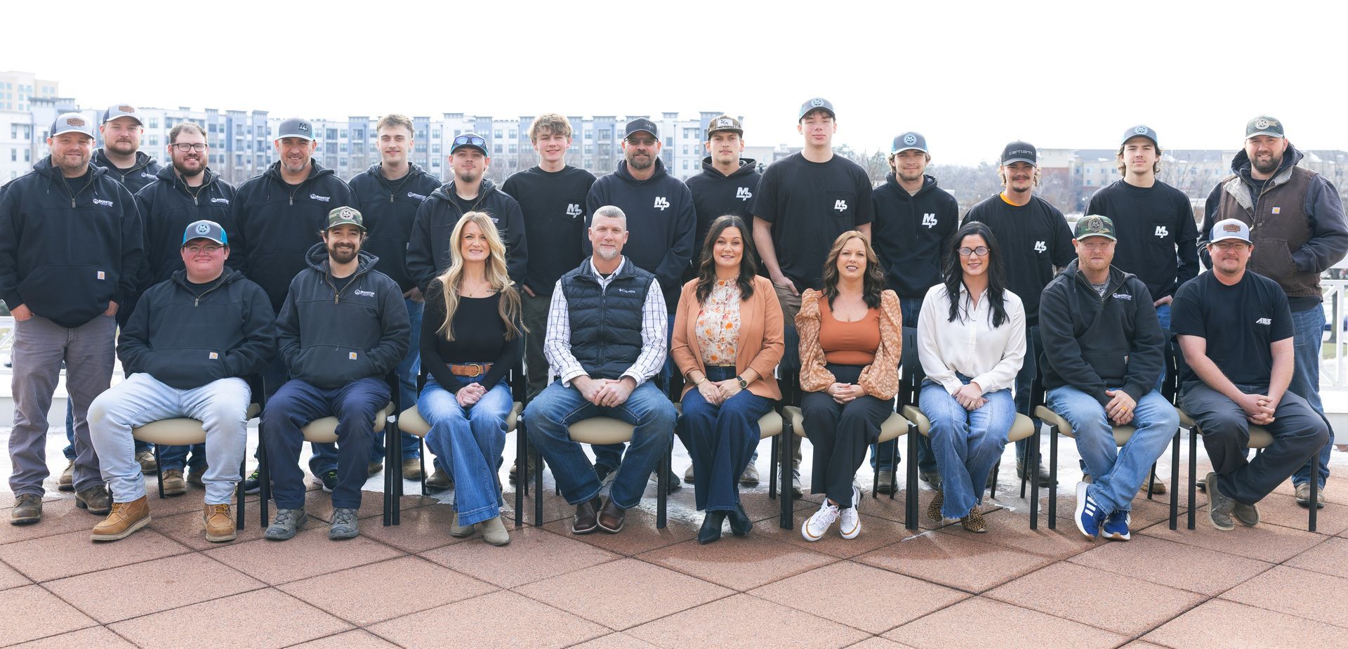 Group of people in casual attire pose in front of a building with windows.