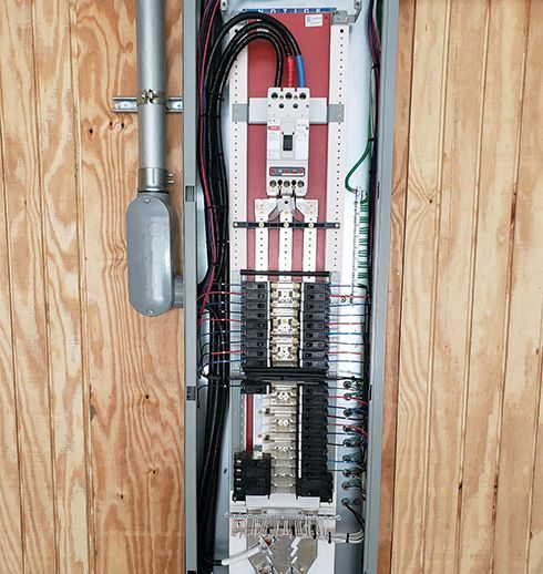 Electrical panel mounted on wooden wall, with wires and circuit breakers visible.