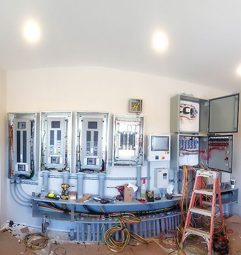 Electrical panel installation: gray panels, wires, tools, ladder, inside a room with overhead lights.
