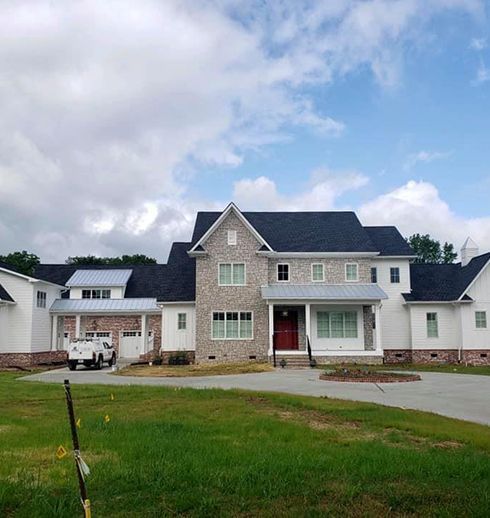 Large two-story house with gray brick, white trim, and dark roof; a white truck sits in the driveway.