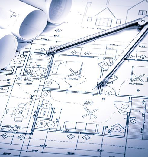 Blueprints of a house with a compass on top, next to rolled-up architectural plans.
