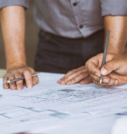 Two people, hands holding pencils, reviewing architectural blueprints.