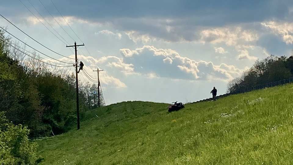 Green hillside with power lines, person and ATV, under cloudy sky.