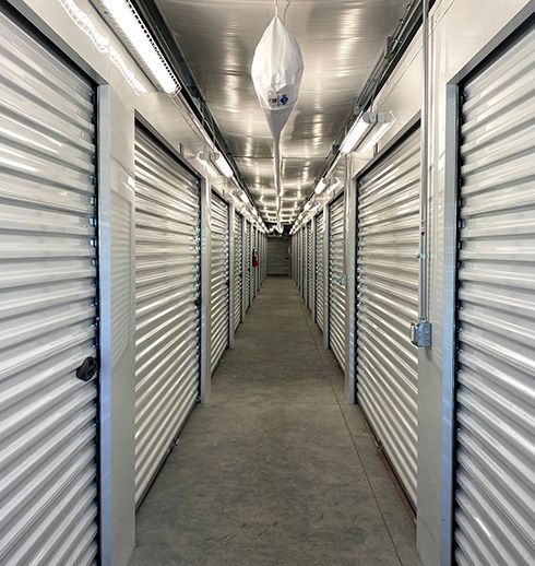 Hallway of storage units with metal doors, bright lighting, and a white ceiling.