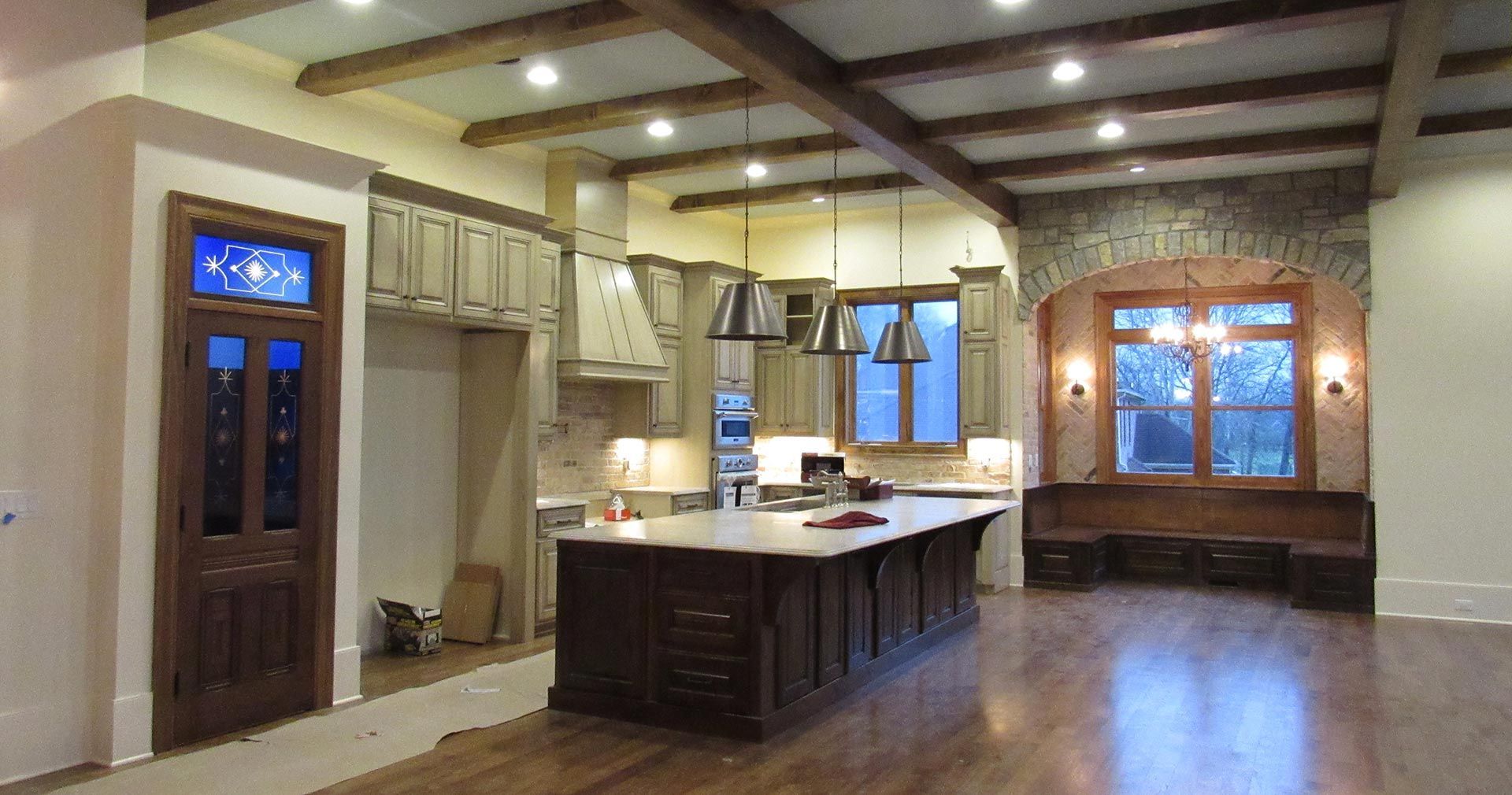 Spacious kitchen with dark island, wood ceiling beams, stone arch, and stained glass door.
