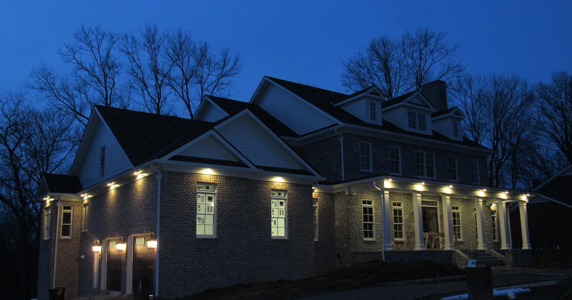 Brick house at night, lit by warm lights; two stories with columns on the porch.