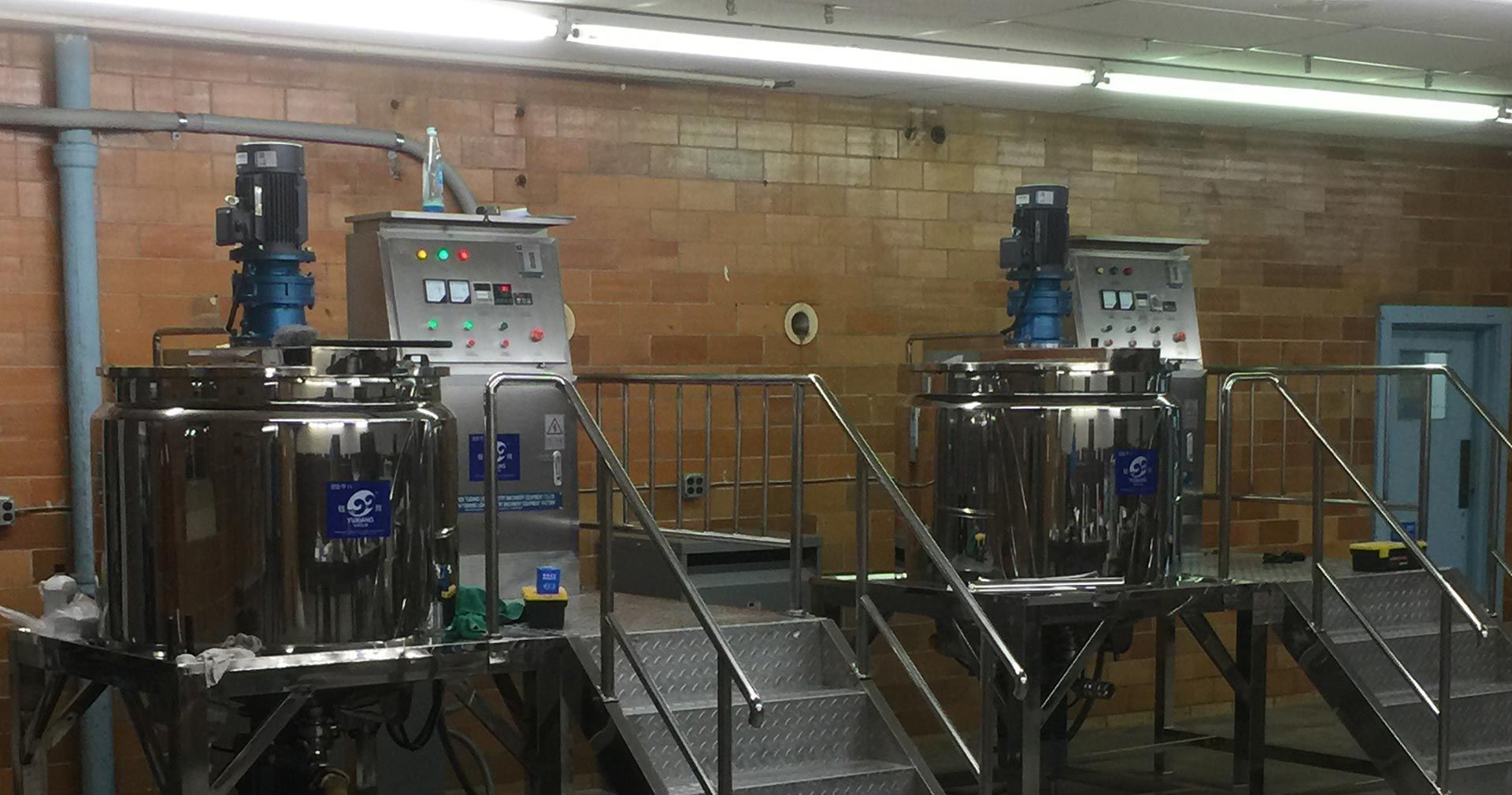 Two stainless steel mixing tanks in a factory setting, with control panels, on elevated platforms.