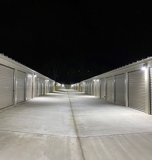 Exterior of a well-lit storage unit facility at night, with rows of closed units.