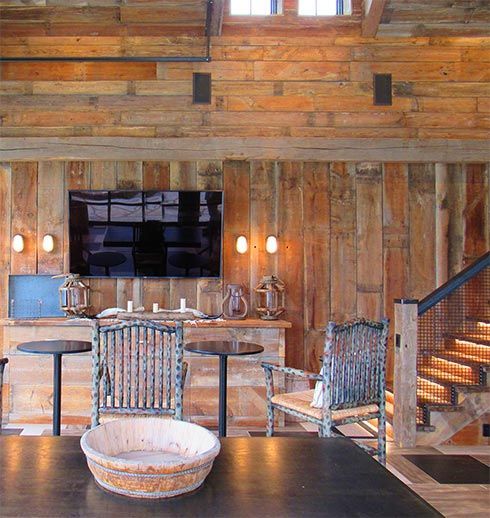 Rustic interior with wood paneling, TV, chairs, and bar. Staircase on right.