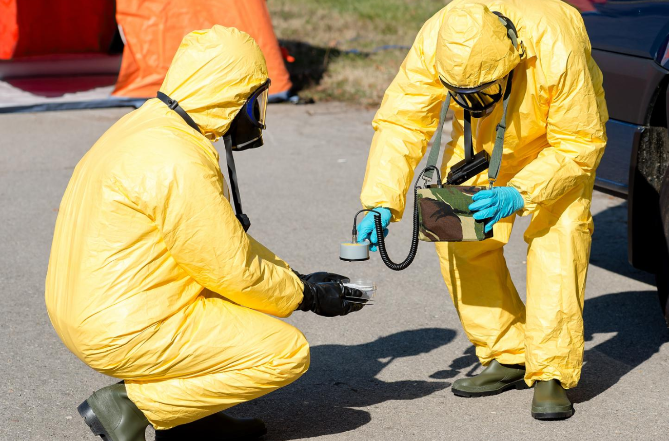 Deux hommes en combinaisons de protection jaunes sont à genoux et regardent quelque chose.