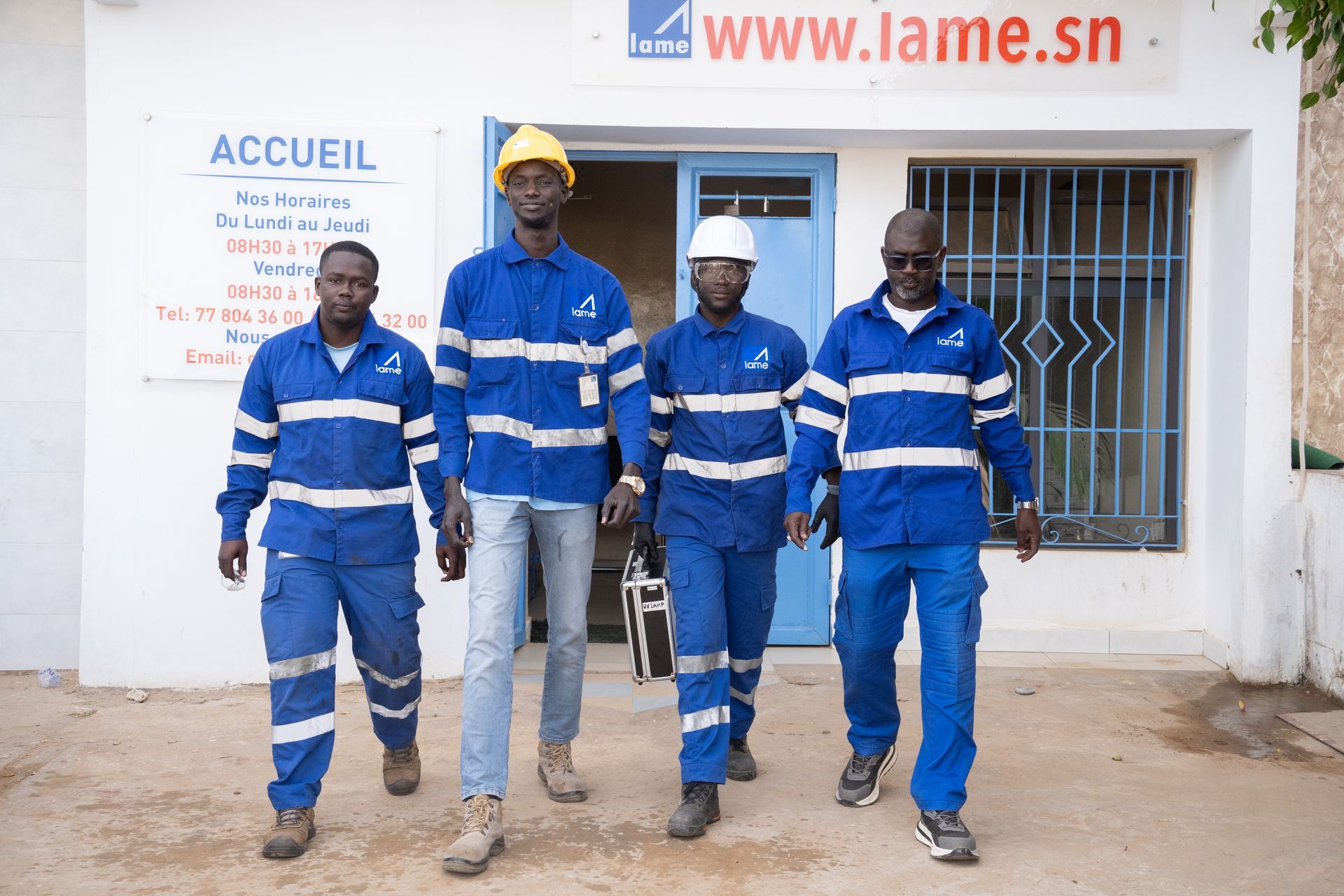 Un groupe d'hommes se tient devant un bâtiment sur lequel est écrit accueil