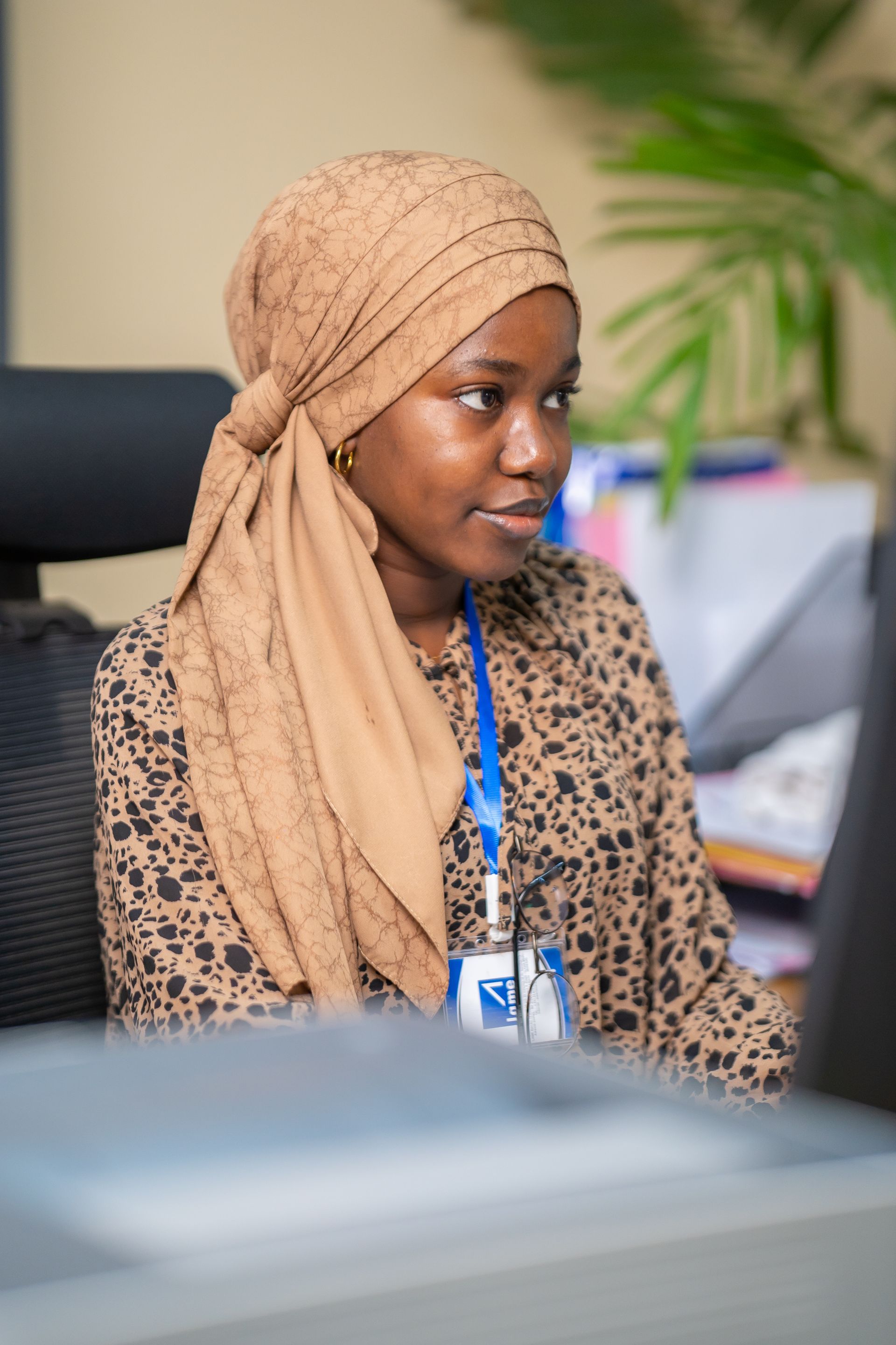 Une femme portant un foulard sur la tête est assise à un bureau devant un ordinateur.