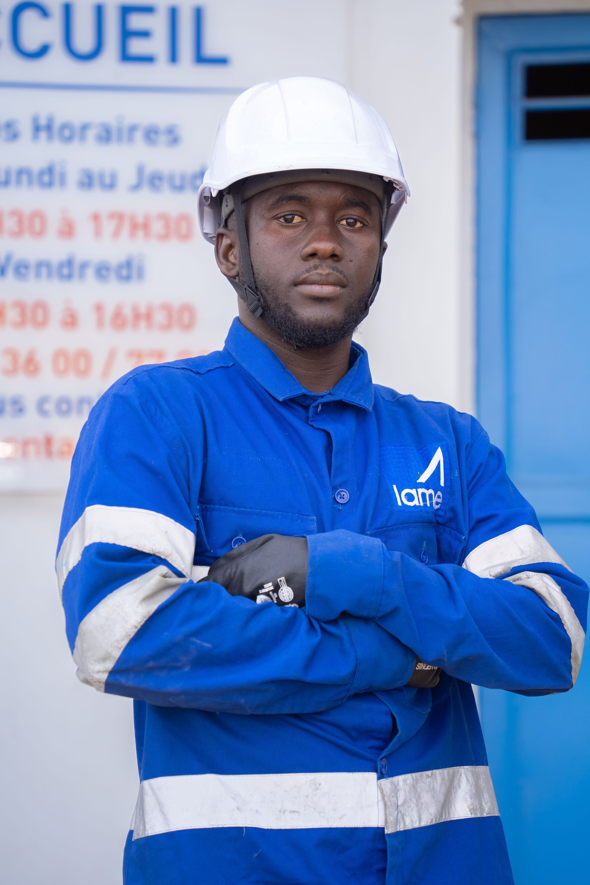 Un homme portant un casque et une chemise bleue est debout, les bras croisés.