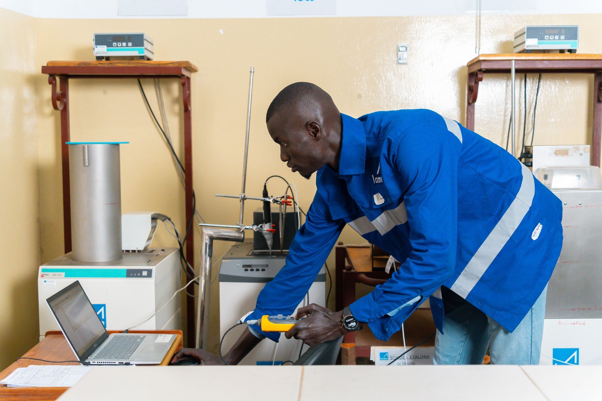 Un homme en veste bleue travaille sur une machine dans un laboratoire.