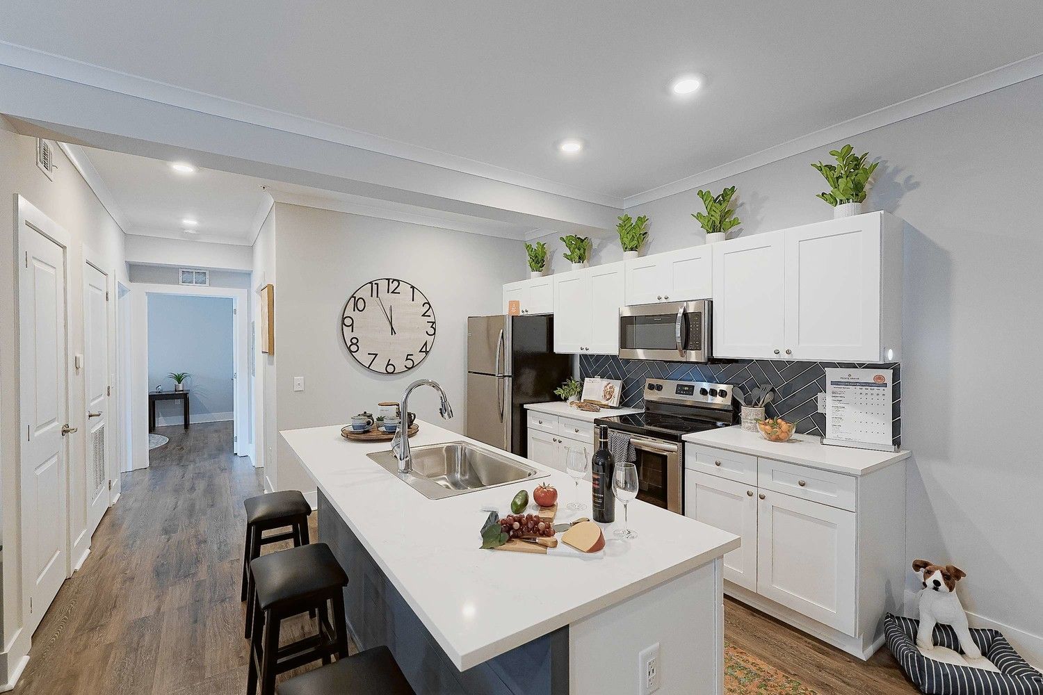 Apartment kitchen with white cabinets, stainless steel appliances, a sink, and a clock on the wall.